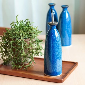 May include: Three blue ceramic bottles with a speckled glaze, two are empty and one is filled with oil, on a wooden tray with a green succulent plant in a terracotta pot.