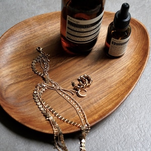 May include: A wooden tray with two amber glass bottles, a gold chain necklace, and a gold ring. The bottles have the text "Aesop" on them.