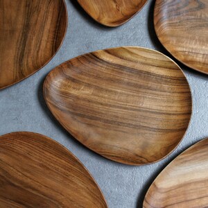 May include: Five wooden serving platters in various sizes and shapes, all with a natural wood grain finish. The platters are arranged on a grey surface.