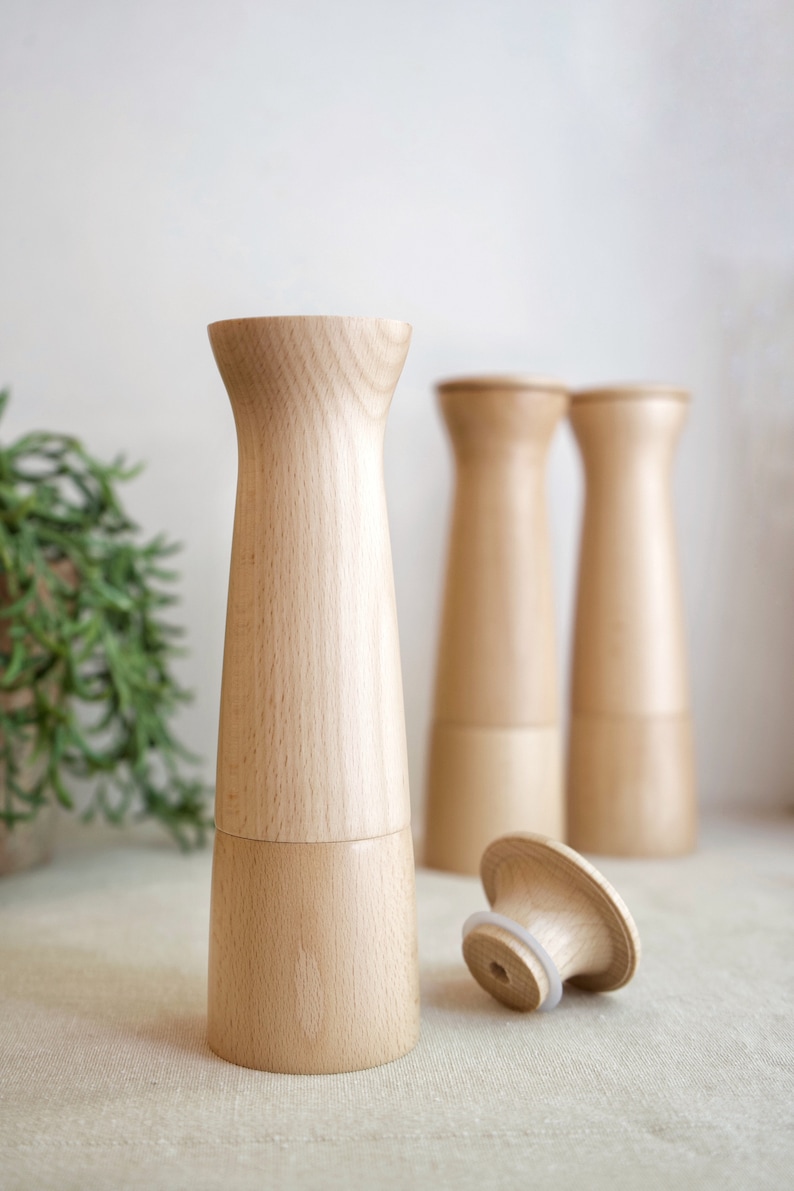 May include: Three wooden salt and pepper shakers with a natural wood finish. The shakers are cylindrical with a slightly flared top and bottom. One shaker is lying on its side with the top off, revealing a white rubber seal.