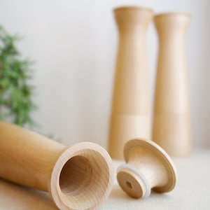 May include: Two wooden salt and pepper shakers with a wooden top and a wooden base. The shakers are in focus, and the top of one shaker is off, revealing the inside of the shaker.