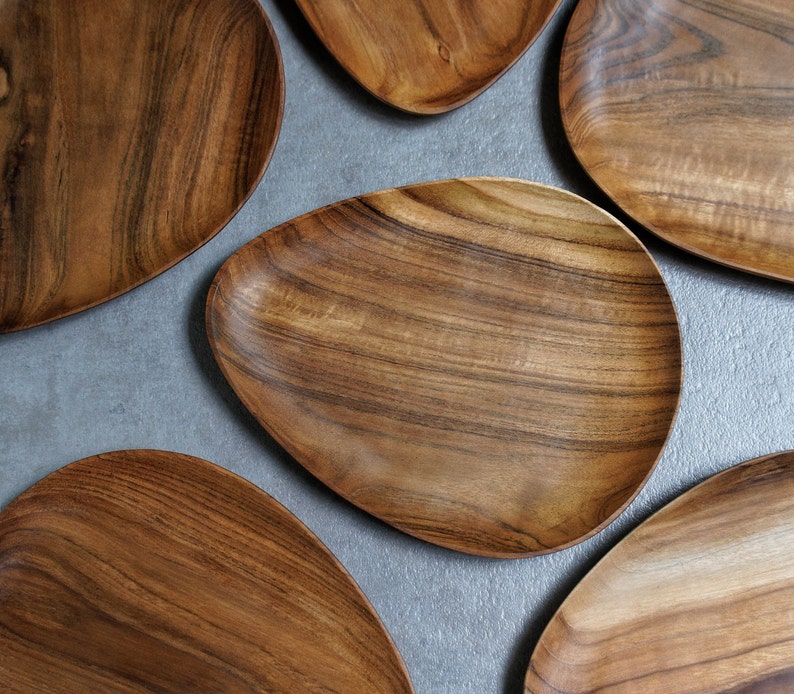 May include: Five wooden serving platters in various sizes and shapes, all with a natural wood grain finish. The platters are arranged on a grey surface.