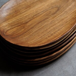 May include: A stack of oval-shaped wooden serving plates. The plates are made of light brown wood with a natural grain pattern.