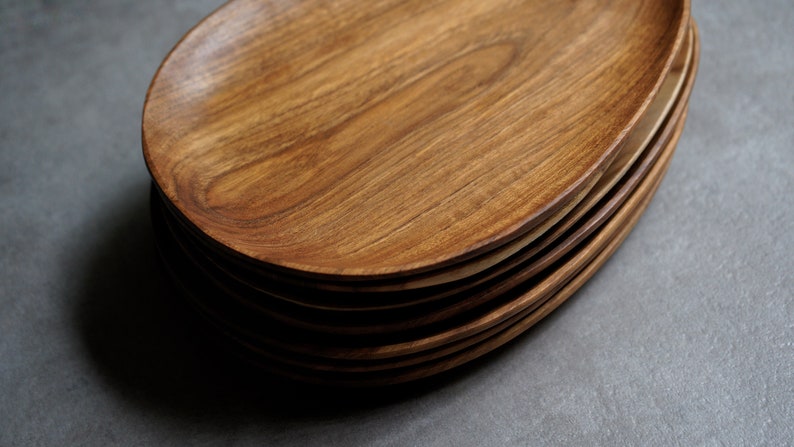 May include: A stack of oval-shaped wooden serving plates. The plates are made of light brown wood with a natural grain pattern.