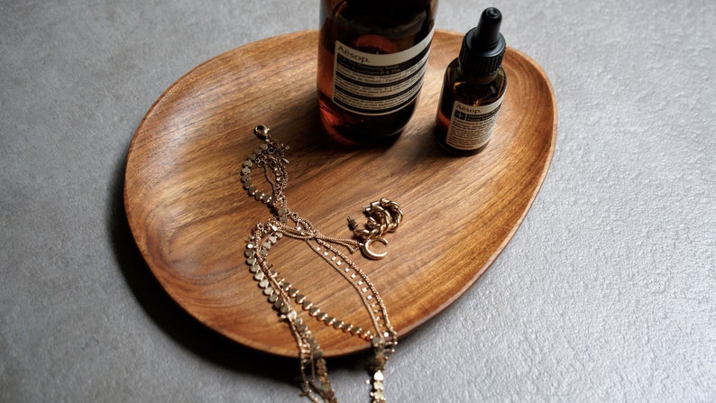May include: A wooden tray with two amber glass bottles, a gold chain necklace, and a gold ring. The bottles have the text "Aesop" on them.