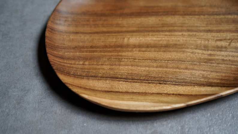 May include: A wooden serving tray with a natural wood grain finish. The tray is oval shaped and has a slightly raised edge.