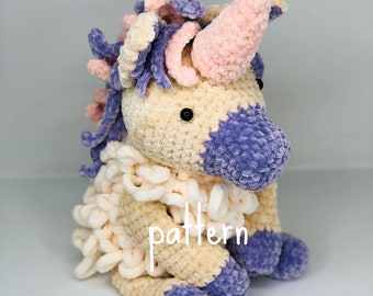 May include: A crocheted unicorn toy with a pink horn, purple and white mane, and purple feet. The unicorn is sitting on a white surface with the word "pattern" written on its body.