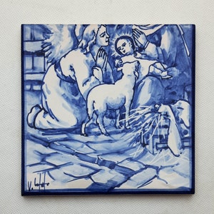 Pu&ograve; includere: Una piastrella di ceramica blu e bianca che raffigura una scena della Nativit&agrave; con un angelo, un agnello e un bambino Ges&ugrave;. La piastrella &egrave; dipinta a mano e ha un aspetto vintage.