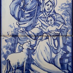 May include: A blue and white ceramic tile depicting the Holy Family. Joseph, Mary, and baby Jesus are depicted in a pastoral setting with a lamb. The tile is painted in a traditional blue and white style.
