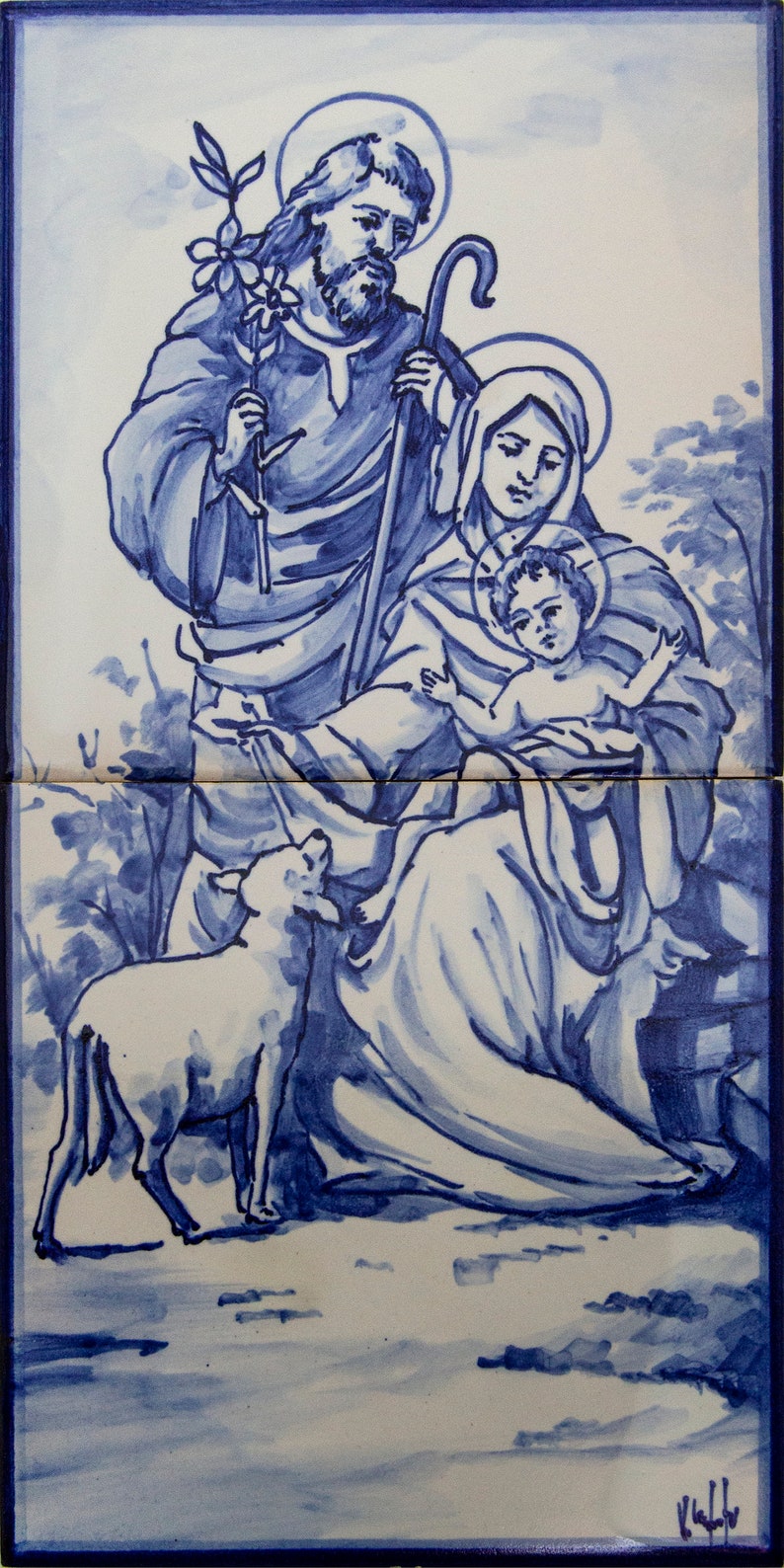 May include: A blue and white ceramic tile depicting the Holy Family. Joseph, Mary, and baby Jesus are depicted in a pastoral setting with a lamb. The tile is painted in a traditional blue and white style.