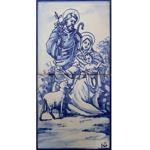 May include: A blue and white ceramic tile depicting the Holy Family. Joseph holds a staff and a sprig of olive branches. Mary holds the baby Jesus. A white lamb is in the foreground.