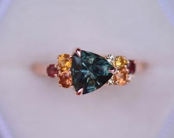 May include: A gold ring with a triangular green gemstone surrounded by smaller yellow, orange, and red gemstones.