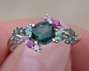 May include: A silver ring with a large green gemstone surrounded by smaller pink and green gemstones.