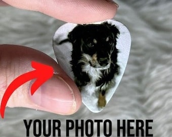May include: White guitar pick with a photo of a black and white dog on it. The text "YOUR PHOTO HERE" is printed below the pick.