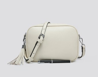 May include: A white leather crossbody bag with a black strap and a tassel. The bag has a rectangular shape and a zipper closure.