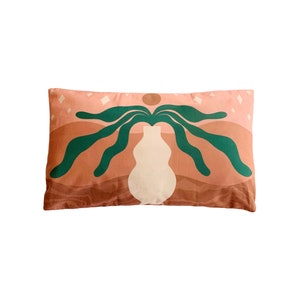 May include: A pink and brown cushion with an abstract green design. The design features a vase with a plant growing out of it. The background is a light pink with white stars.