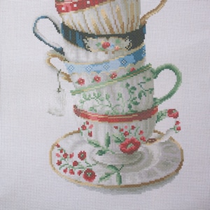 May include: A stack of six decorative teacups and a saucer, each with unique patterns and colors. The cups feature gold accents, floral designs, and bands of red, blue, and black. The teacups are stacked on top of each other.