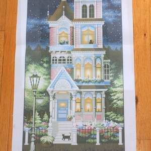 May include: A needlepoint canvas featuring a detailed illustration of a Victorian-style house with a blue door, lit windows, and a black cat in the front yard. The canvas includes a color chart with 40 different colors.