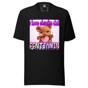 Puede incluir: Camiseta negra con un gráfico de un oso de peluche sosteniendo un corazón y un pincel, con el texto "i love chiefin dat" y "FENTJAMIN" en una fuente colorida. La camiseta está hecha de un material suave.
