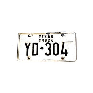 May include: A weathered Texas truck license plate. The plate is white with black lettering, displaying the text "TEXAS TRUCK" and the registration number "YD 304". The plate shows signs of age and wear.