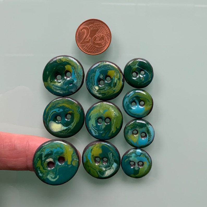 Puede incluir: Surtido de diez botones con estampado de remolino verde, azul y blanco. Los botones tienen dos agujeros cada uno.