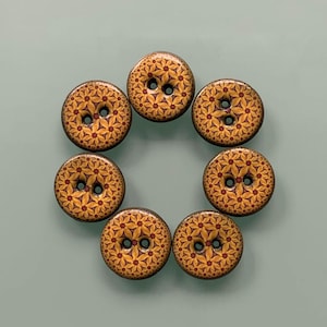Könnte beinhalten: Ein Set aus sieben runden Knöpfen, die in einem Kreis angeordnet sind. Jeder Knopf zeigt ein sich wiederholendes geometrisches Blumenmuster in Gelb-, Orange- und Dunkelrottönen. Jeder Knopf hat zwei mittige Löcher und einen glatten Rand.