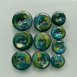 Puede incluir: Un conjunto de nueve botones de cer&aacute;mica con un dise&ntilde;o marmoleado en tonos de verde, azul y amarillo. Los botones tienen dos agujeros cada uno.