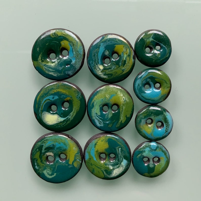 Puede incluir: Un conjunto de nueve botones de cer&aacute;mica con un dise&ntilde;o marmoleado en tonos de verde, azul y amarillo. Los botones tienen dos agujeros cada uno.