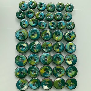 Puede incluir: Una colecci&oacute;n de 36 botones con estampado de remolino verde y azul. Los botones son todos del mismo tama&ntilde;o y forma, y est&aacute;n dispuestos en un patr&oacute;n de cuadr&iacute;cula.