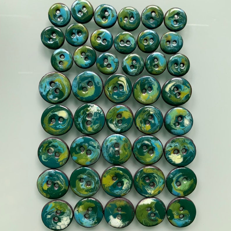 Puede incluir: Una colecci&oacute;n de 36 botones con estampado de remolino verde y azul. Los botones son todos del mismo tama&ntilde;o y forma, y est&aacute;n dispuestos en un patr&oacute;n de cuadr&iacute;cula.