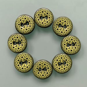 Könnte beinhalten: Ein Set aus acht runden Knöpfen, die in einem Kreis angeordnet sind. Jeder Knopf hat eine hellgelbe Grundfarbe mit einem sich wiederholenden schwarzen geometrischen Muster aus kleinen Dreiecken und Punkten. Jeder Knopf hat zwei Löcher.