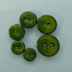 Könnte beinhalten: Sechs grüne Keramikknöpfe mit jeweils zwei Löchern. Die Knöpfe haben eine dunkelgrüne Glasur mit einem marmorierten Effekt.