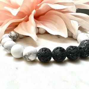 May include: A bracelet made of white and black beads. The white beads are round and smooth, while the black beads are rough and textured. The bracelet is lying on a white surface.
