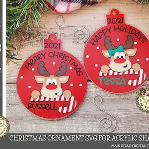May include: Two red and white Christmas ornaments featuring a cartoon reindeer with a candy cane. The ornaments are personalized with the names "Russell" and "Tessa" and the year "2021". One ornament says "Merry Christmas" and the other says "Happy Holidays".
