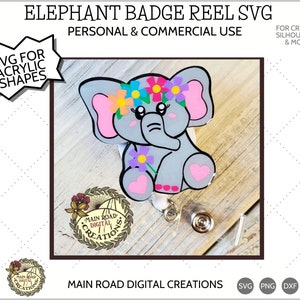 May include: A gray elephant badge reel with a pink flower crown and pink heart accents. The elephant is sitting on a wooden surface with a badge reel attached to its back. The text "MAIN ROAD DIGITAL CREATIONS" is visible below the elephant.