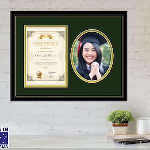May include: A black framed certificate with a gold border and a green background. The certificate has a gold seal and the text "Certificate of Achievement". A photo of a person wearing a graduation cap and gown is in the top right corner of the frame.