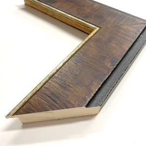 May include: Close-up of a wooden picture frame with a dark brown finish and a gold trim. The frame has a beveled edge and a textured surface.