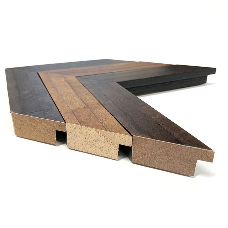 May include: Close-up of a corner of a multi-layered picture frame. The frame is made of wood with a dark brown, light brown, and natural wood finish.