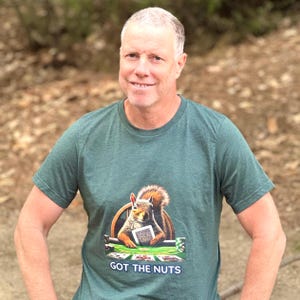 Puede incluir: Camiseta verde con un diseño de una ardilla jugando al póquer y el texto "GOT THE NUTS". La ardilla sostiene cartas en una mesa de póquer. La camiseta la lleva una persona con pelo corto y gris.