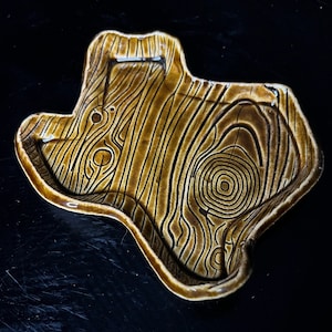 May include: A brown ceramic dish shaped like the state of Texas with a wood grain pattern.