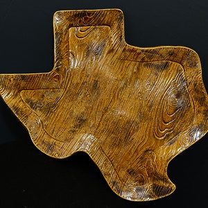 May include: A gold-colored ceramic serving tray shaped like the state of Texas. The tray has a wood-grain pattern and is perfect for serving snacks or appetizers.