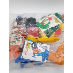 May include: A plastic bag filled with plush toys featuring characters from Kellogg's Breakfast cereals. The characters include Toucan Sam, Snap, Crackle, and Pop, and the rooster from Frosted Flakes. The bag includes the text "Bean Bag Bunch" and "Kellogg's Breakfast Bunch".