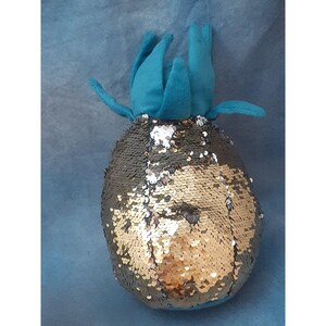 May include: A plush pineapple toy with a teal green top and gold and silver sequins covering the body.