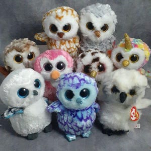 May include: A collection of plush owl toys in various colors, including white, brown, pink, and blue. Each owl has large, round eyes and a soft, fluffy texture. Some owls have unique features like a horn or patterned feathers.