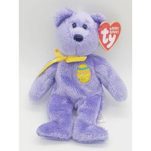 May include: Purple plush Easter-themed beanie baby with a yellow ribbon and an embroidered Easter egg on its chest. The tag reads "Basket Beanies Ty".