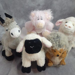 May include: Five plush animal toys: a gray donkey, a pink pig, a white sheep, a black and white lamb, and a brown and gray hedgehog. The toys are soft and cuddly, with embroidered details and varying textures.
