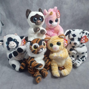 May include: A collection of plush animal toys, including a cow, a cat, a tiger, a dalmatian, a Siamese cat, and a unicorn. Each stuffed animal has large, expressive eyes and a Ty heart-shaped tag.
