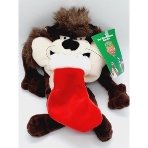 May include: A plush Tazmanian Devil character with a red Christmas stocking. The plush toy has brown fur, a white face, and a red stocking with a white cuff. A green tag reads "Taz with stocking bean bag".