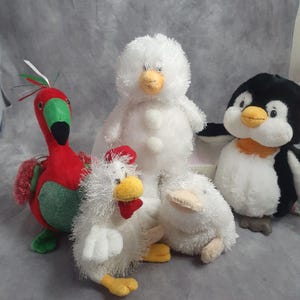 May include: A collection of plush toys featuring a red parrot, a white snowman, a white chicken, a white duck, and a penguin. The parrot has green and red accents. The snowman has three white buttons. The penguin has a black body and white belly.