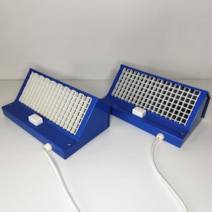 May include: Two blue desk lamps with white gridded diffusers. Each lamp has a white switch and a white cord. The lamps are angled and sit on a white surface.